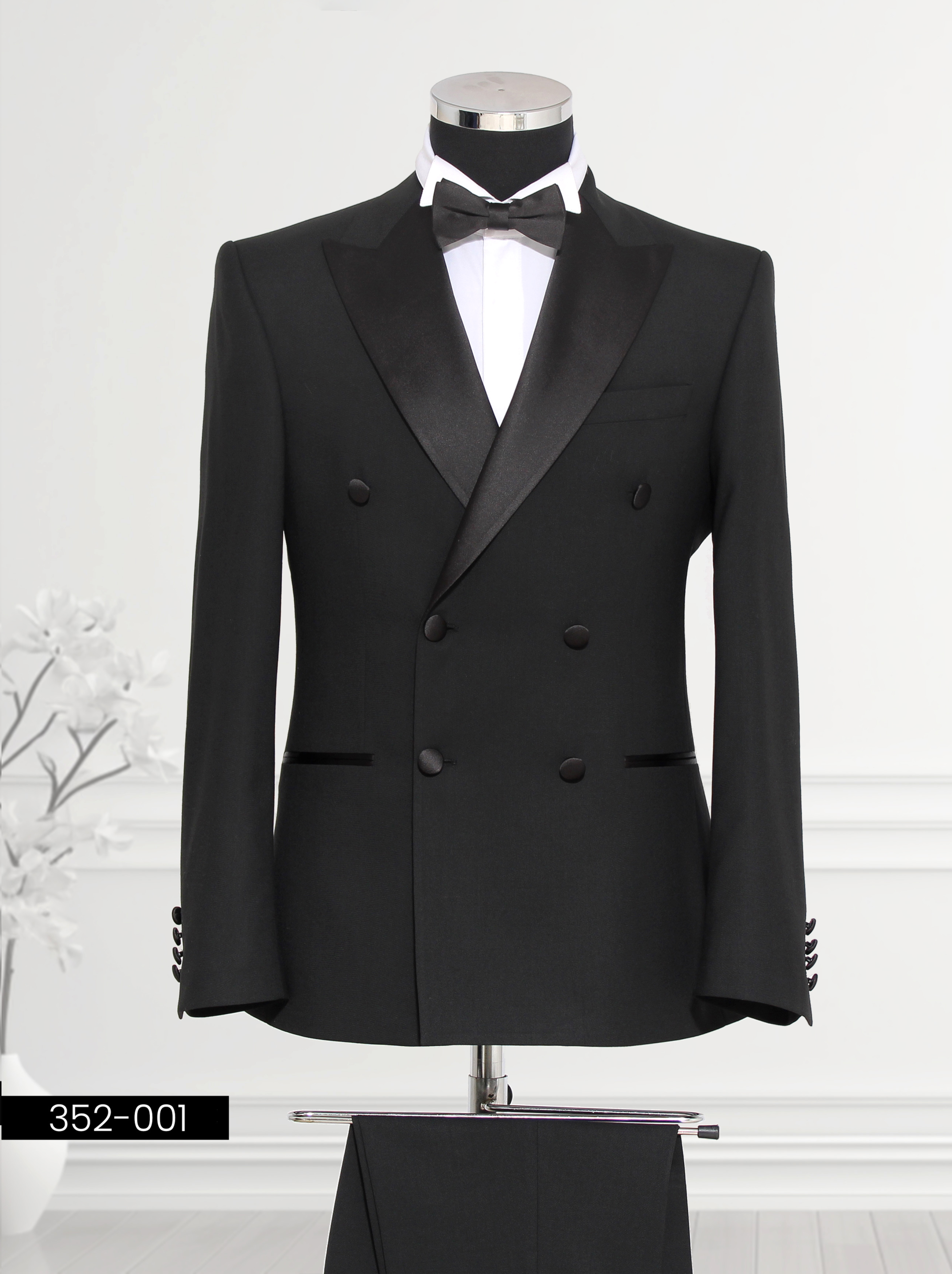 A black double-breasted tuxedo with a satin lapel and bow tie, displayed on a mannequin.